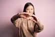 © Krakenimages.com - Young beautiful asian woman wearing fashion and elegant sweater over pink solated background smiling in love doing heart symbol shape with hands. Romantic concept.