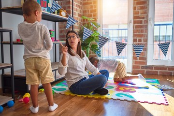 Beautiful teacher angry poiting with finger to toddler around lots of toys at kindergarten