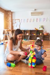 Poster - Young beautiful teacher and toddler playing with building blocks toy at kindergarten