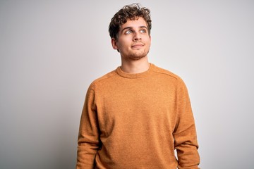 Wall Mural - Young blond handsome man with curly hair wearing casual sweater over white background smiling looking to the side and staring away thinking.