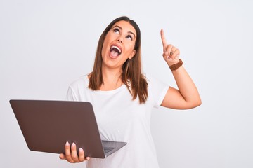 Poster - Beautiful young woman working using computer laptop over white background smiling amazed and surprised and pointing up with fingers and raised arms.