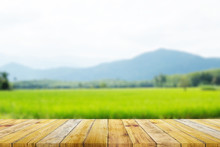 Shelf Of Brown Wood Plank Board With Blurred Green Rice Field Farm With Mountain And Hut Nature Background.