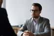 © fizkes - Serious businessman with clasped hands looking at opponent at negotiations