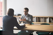© fizkes - Two businessmen having conversation, sitting at table in boardroom