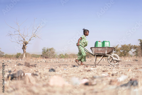 Photographie Little African Woman Transporting Fresh Water as a drought symbol