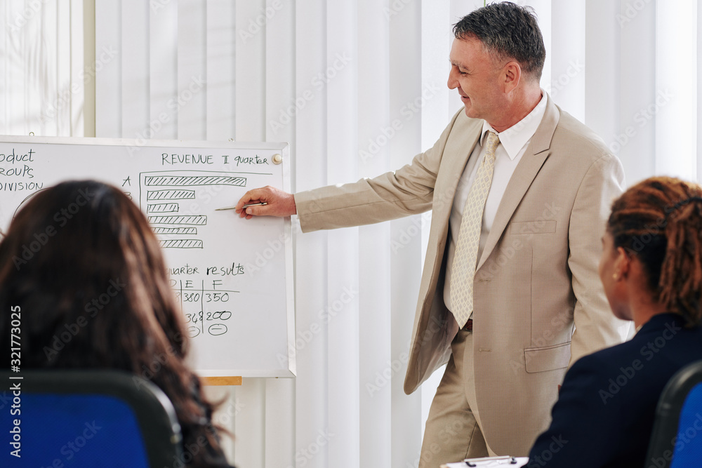 Mature business executive pointing at chart on whiteboard and talking ...