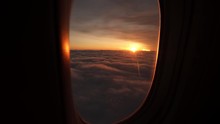 View From Plane Window Sunshine Clouds. Looking Through Window Aircraft During Flight In Wing At Sunset Or Sunrise. Clouds, Sun And Sky Through Window Of Airplane. Travel Tourizm Trip. 4 K Slow-mo