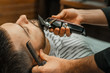 © Natalya Lys - Beauty shop for men. Shaving a beard in a barbershop. Barber cuts his beard with a razor and clipper. close up Brutal haircuts. Hairdresser equipment. Selective focus.