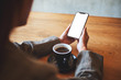 © Farknot Architect - Mockup image of a woman holding black mobile phone with blank screen with coffee cup on wooden table