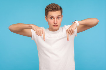 Come to me here now! Portrait of bossy man in white t-shirt pointing fingers down, demanding approach to him immediately, having control over situation. indoor studio shot isolated on blue background