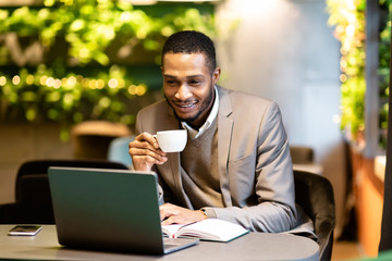 Wall Mural - Afro guy drinking tea and using personal computer