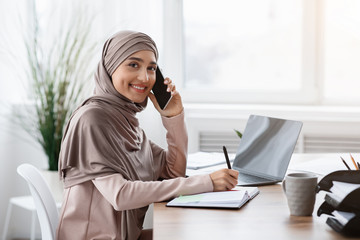 Wall Mural - Arabic Female Secretary Talking On Cellphone And Taking Notes In Office