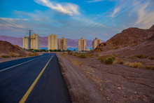 Outskirts Car Road To Eilat Israeli City Urban Country Side View With Sand Stone Rocks Foreground And Living Buildings Background In Soft Colors Twilight Lighting Evening Time