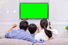 Back View Of Happy Asian Family Watching TV Together In Living Room At Home; Cheerful And Fun With Movie, With Green Screen