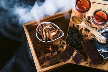 Chinese tea ceremony. Glass tea cups with the famous chinese red black tea with vapour smoke on a black background. Chocolate, honey and dried pear snacks