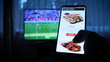 © dkHDvideo - Background of the TV at home (at the bar), the guy orders different snacks, pizza and sweets scrolling through internet stores using mobile phones. Concept: Sport TV.