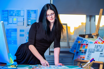 Wall Mural - a girl in a black dress standing at the table in the office. the girl is passionate about her work. 