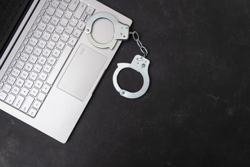 Handcuffs and laptop on dark background top view. Piracy, internet hacking and punishment for cybercrime concept.