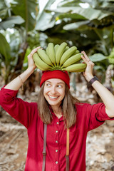 Wall Mural - Portrait of a cute smiling woman holding a stem with fresh green bananas above the head. Healthy eating and wellness concept