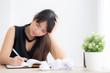 © NT_studio - Beautiful asian woman tired and stressed with writing overworked at desk, girl with worried not idea with notebook and crumpled paper at office, freelance and business concept.