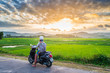 © fabio lamanna - One person on motorbike looking at view of rice fields and mountains in the Phu Yen province, Nha Trang Quy Nhon, adventure traveling in Vietnam. Rear view sunburst backlight dramatic sky at sunset.