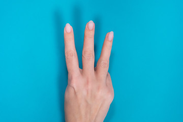 Beautiful female manicured hand isolated on blue background showing 3 fingers up.