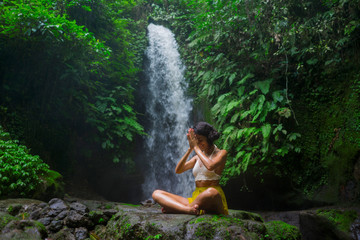 outdoors portrait of young attractive and happy hipster woman doing yoga at beautiful tropical waterfall meditating enjoying freedom and¡ nature in wellness and zen lifestyle