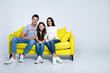 © My Ocean studio - Together forever. Portrait of a beautiful happy family sitting on a yellow couch at home in their living room.