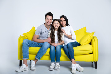 Like mother, like daughter. Husband, wife and daughter are sitting and hugging on the couch, looking in the camera with big smiles.