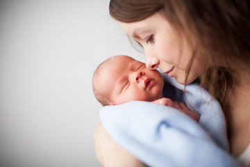 close up of beautiful young woman holding adorable baby wrapped in blue blanket. cute child sleeping