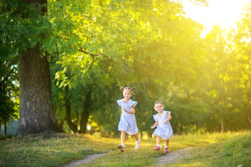 Wall Mural - Cute children are walking in the park at sunset. Girls run along the path and have fun. Children play and have fun outdoors.