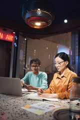 Wall Mural - vertical portrait of two ethnic business people working late in dark office, copy space