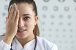 © H_Ko - Eye examination by specialist in eye disease. Young woman doctor in white coat closes one eye with his hand. Detection disease and early diagnosis with regular examination by an ophthalmologist.