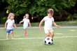© AMR Studio - Football game: team of toddlers playing soccer on green field: three children, two boys (one is barefoot) and girl playing at stadium, smiling little boy dribbling ball is running in front place