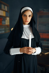 Young nun in a cassock holds a candle