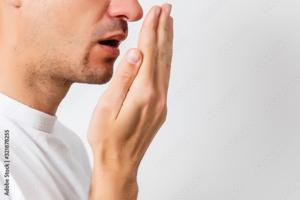Bad breath. Halitosis concept. Young man checking his breath with his hand. - obrazy, fototapety, plakaty 