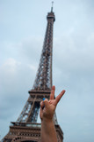 Fototapeta Paryż - Hand making the peace symbol in front of the Eiffel tower in Paris, France