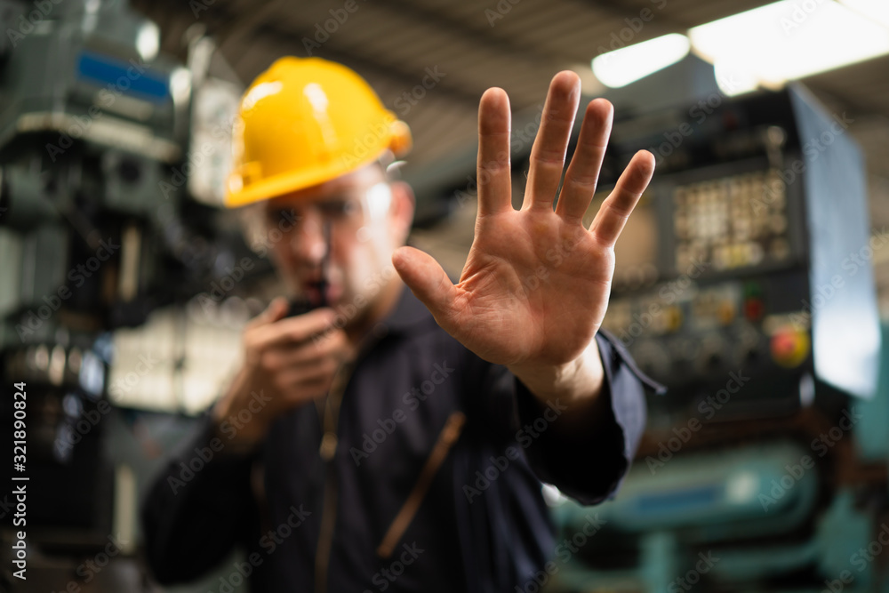 Industrial worker in factory site gesture keep out or stop while communicating with a walkie talkie. - obrazy, fototapety, plakaty 