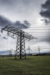 Sun hidden behind dramatic clouds and electricity pylons conducting current from distribution power station, solar renewable energy and grid stability concept, copy space