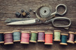 Row of vintage wooden spools of multicolored threads, tailoring scissors, thimbles, measuring tape, sewing items on wooden board. View from above.