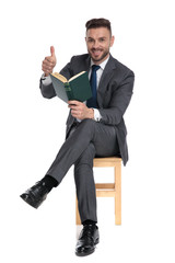 Canvas Print - happy young man holding book and making thumbs up sign