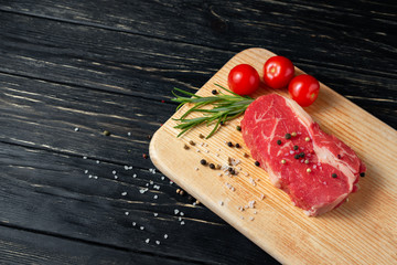 Wall Mural - One pieces of juicy raw beef on a cutting board on a black wooden table background.