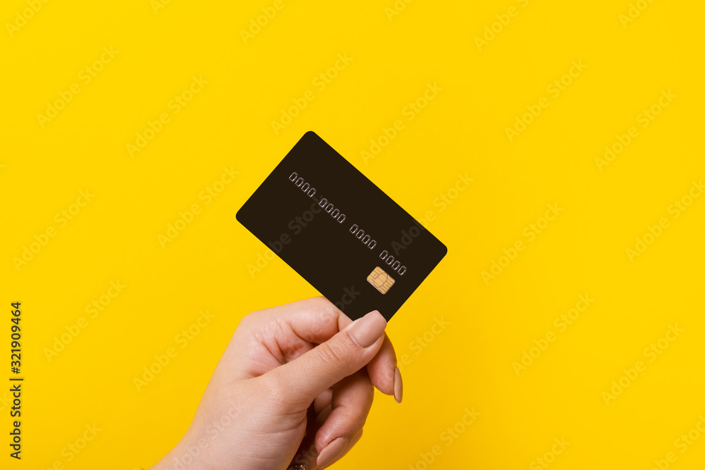 Female hand holding credit card on yellow background - obrazy, fototapety, plakaty 