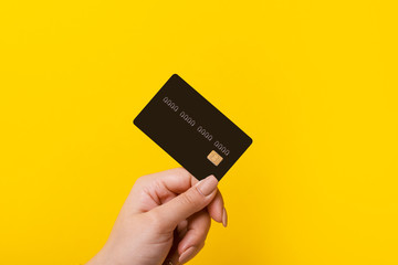 female hand holding credit card on yellow background