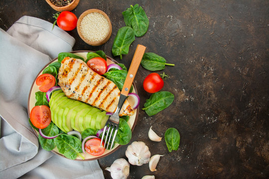 Grilled chicken breast and fresh vegetable salad with spinach leaves, avocado and tomatoes on a dark background. Salad of greens with meat. Ketogen diet. Dietary nutrition. Copy space. 
