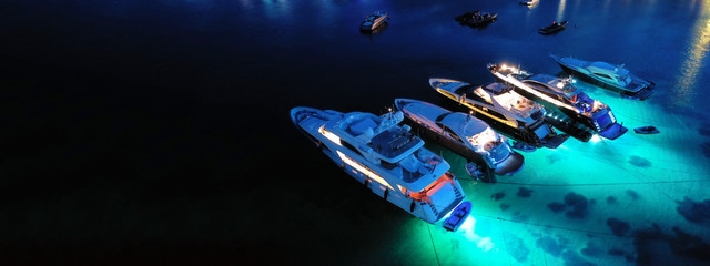 Aerial drone night shot of luxury yachts docked famous Psarou beach, Mykonos island, Cyclades, Greece
