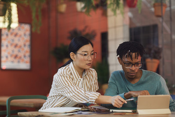 Wall Mural - portrait of two ethnic young people working on project together while sitting at table in cafe, copy