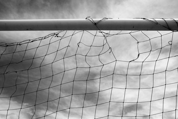 Ripped and torn football net hangs from its top bar in this black and white photo