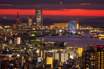 Canvas Print - Japan. Osaka city in the evening. Osaka Bay under a black and red sky. Sunset over the Japanese city. Ferris wheel in Osaka. Ferris wheel with evening illumination. Ferris Wheel Tempozan.