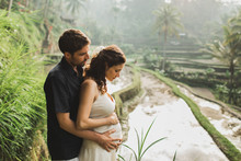 Young Latin Pregnant Woman With Husband With Amazing View Of Ubud Rice Terraces. Pregnant Couple Happy Together.